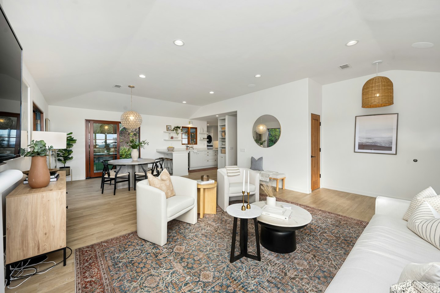 Modern open-concept living, dining, and kitchen area with light wood floors.